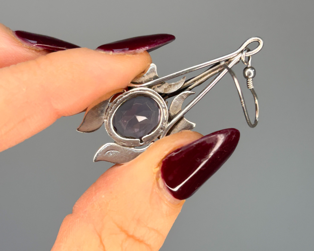 Art nouveau silver and amethyst earrings, held up by woman's hand, showing reverse of the earring