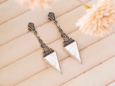 art deco style mother of pearl earrings in silver with marcasite stones, shown on a pink tray