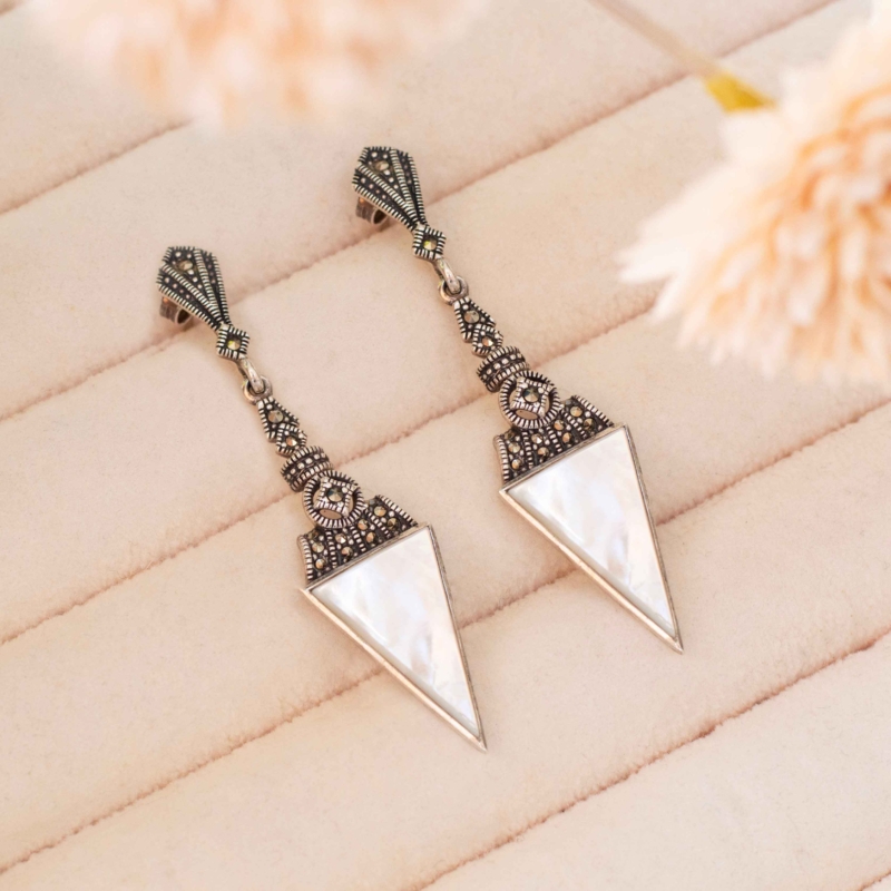 art deco style mother of pearl earrings in silver with marcasite stones, shown on a pink tray