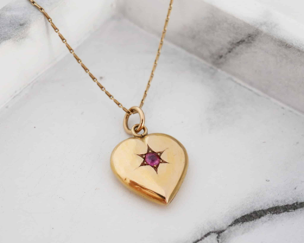 ruby-heart-pendant-5.jpg Victorian 16ct gold and ruby heart pendant on gold chain laying on marble