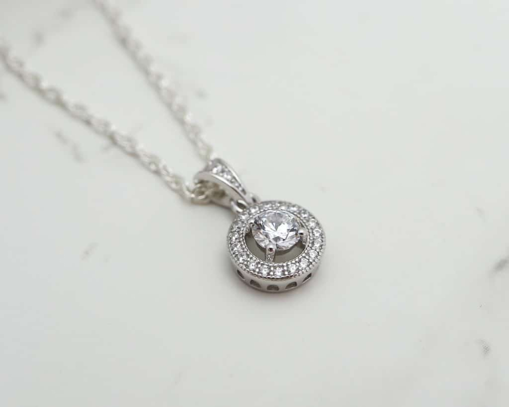 silver and CZ halo pendant on a chain flat lay