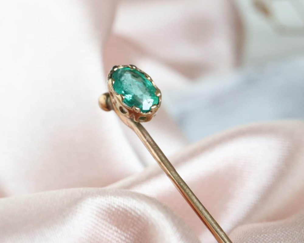 antique 9ct gold stick pin with green stone on pink fabric
