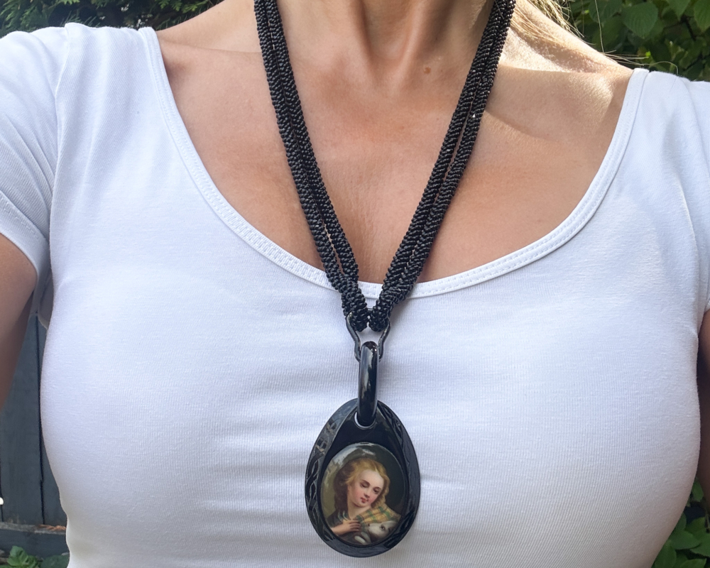 antique Victorian Whitby Jet beads with pendant hanging from them showing the image of a person in Victorian times, worn on a lady's neck