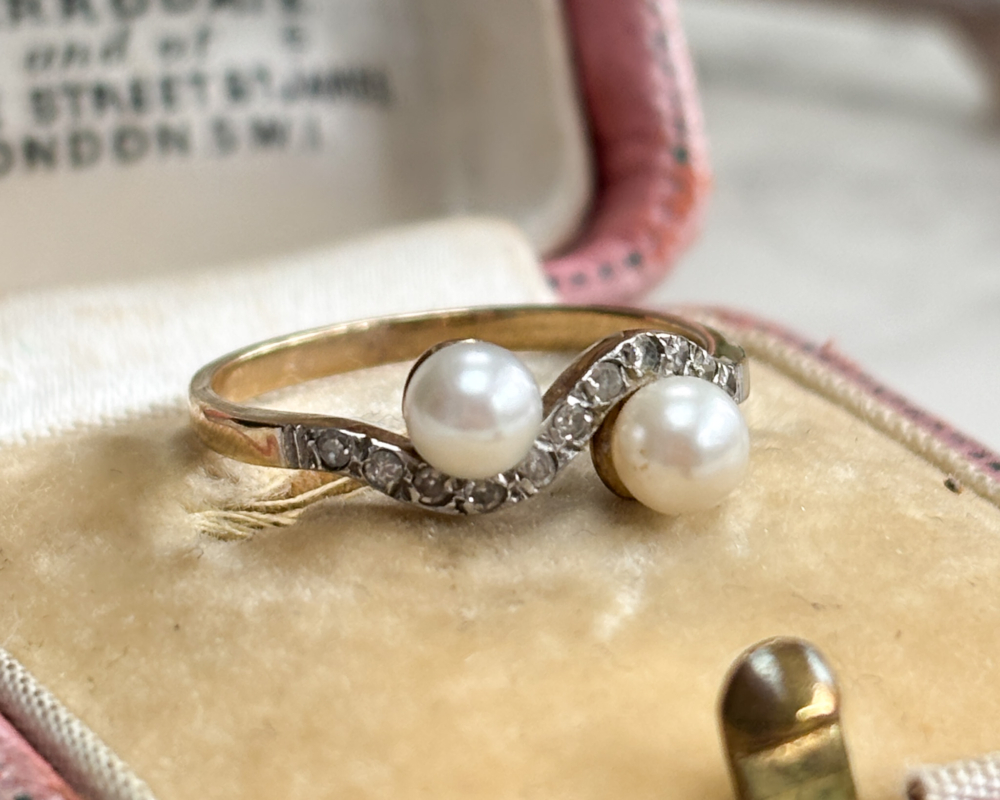 antique Edwardian pearl toi et moi ring set with diamonds, shown on top of a pink box