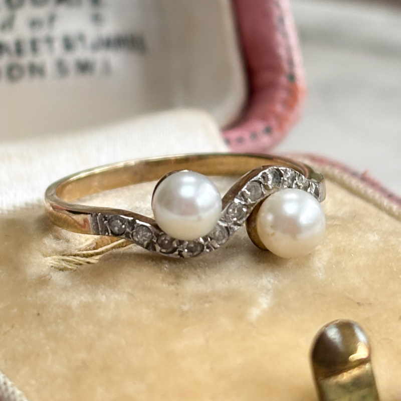 antique Edwardian pearl toi et moi ring set with diamonds, shown on top of a pink box