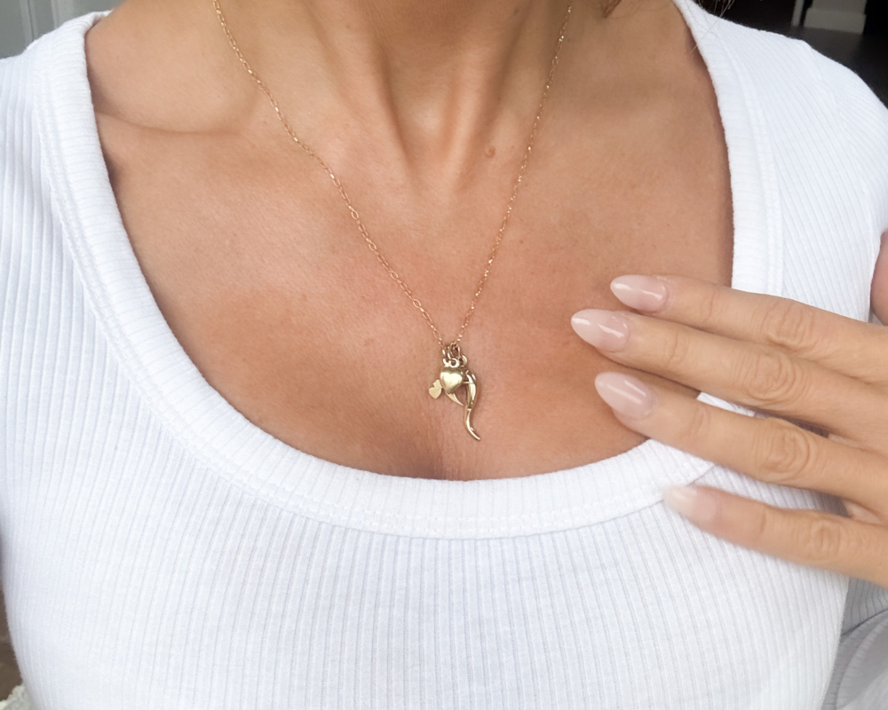 vintage 9ct gold charm necklace with heart charm, horn of plenty and bird on a gold chain. Shown on woman's neck