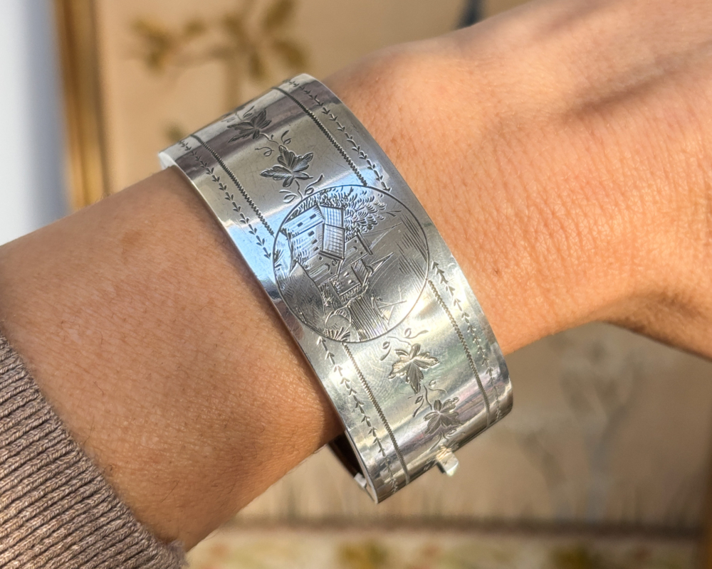 Victorian silver bangle depicting rural church scene for sale, shown on woman's wrist