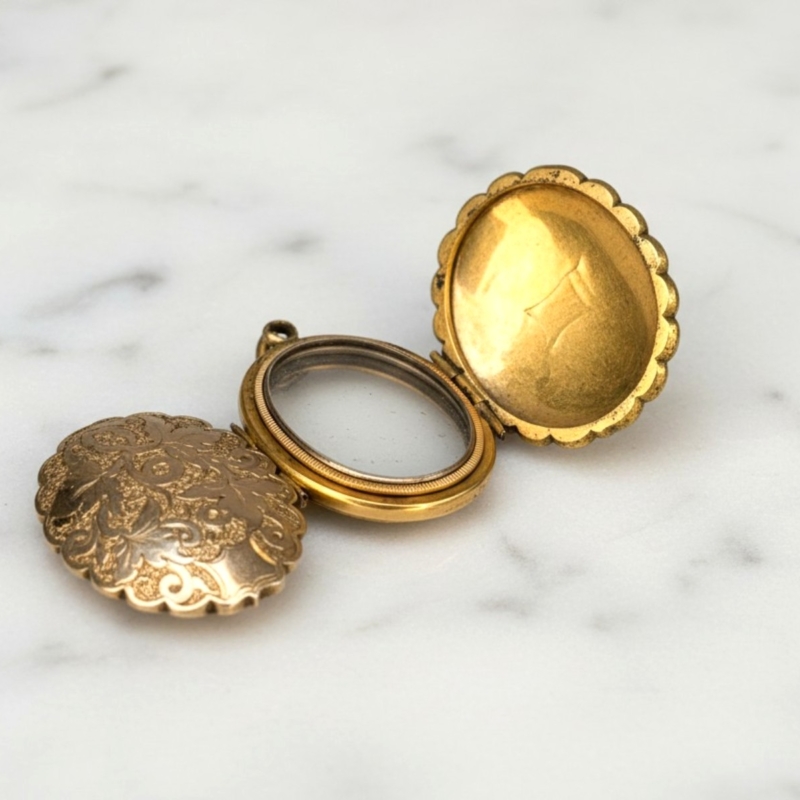 antique Edwardian fanily locket made from pinchbeck with scrolled chased detail, open to reveal compartments, laying on marble background