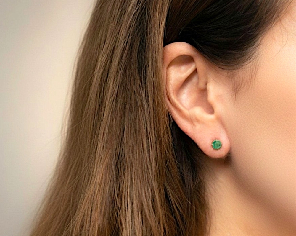 modern round claw set emerald studs in 9ct yellow gold for sale in Leeds, shown on a model's ear