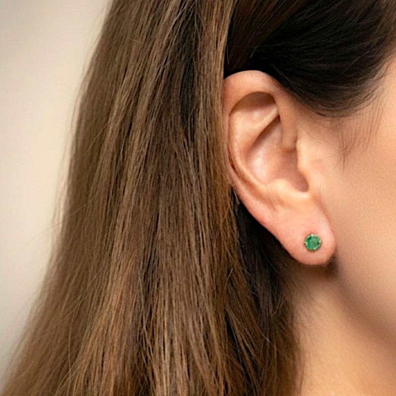 modern round claw set emerald studs in 9ct yellow gold for sale in Leeds, shown on a model's ear