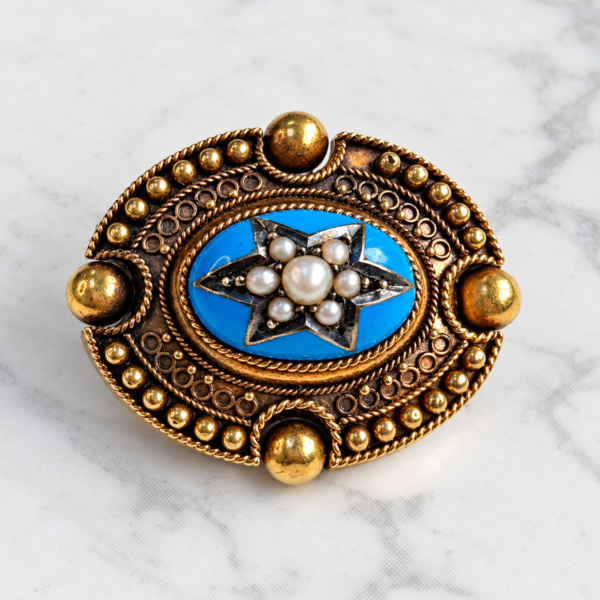antique Victorian Etruscan Revival gold and enamel brooch with seed pearls in a star setting. Displayed on marble