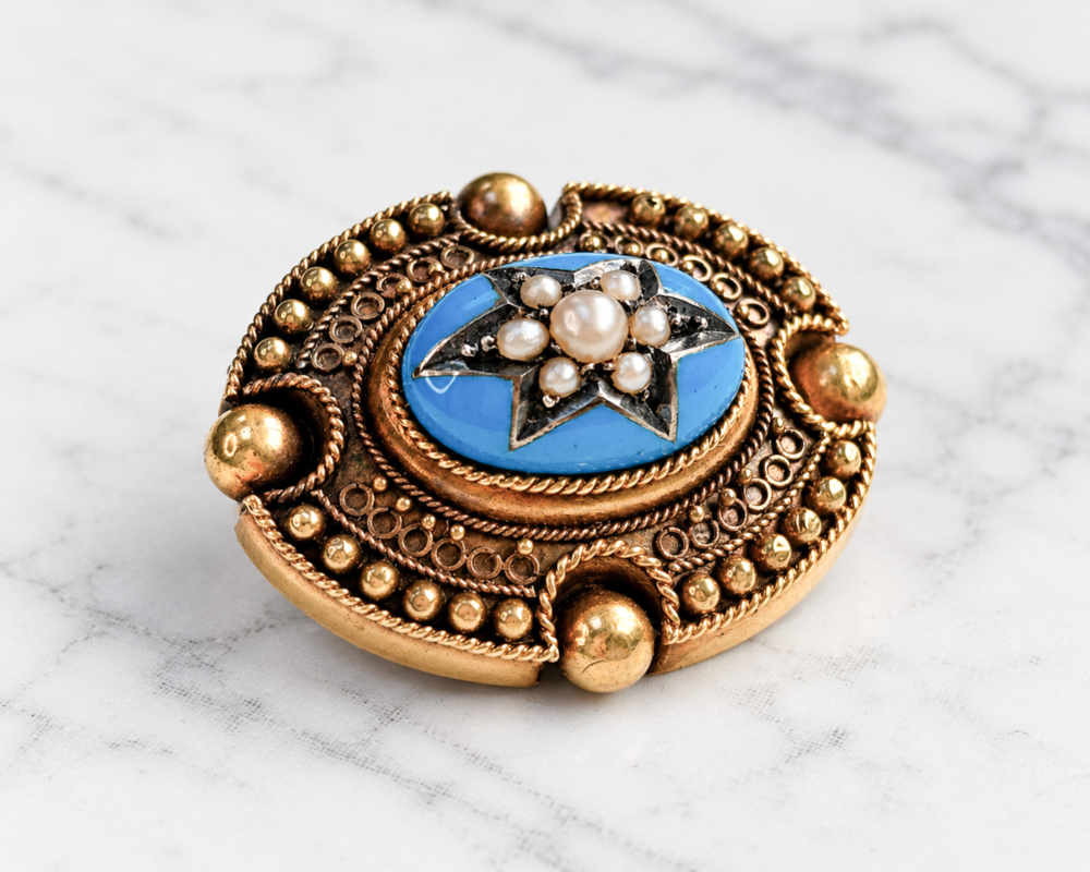antique Victorian Etruscan Revival gold and enamel brooch with seed pearls in a star setting, displayed on a marble background