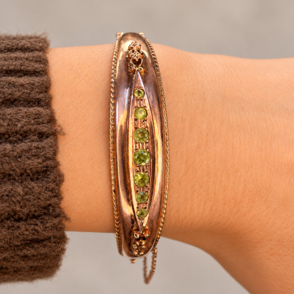 vintage 9ct rose gold peridot bangle worn on a wrist wearing a brown jumper