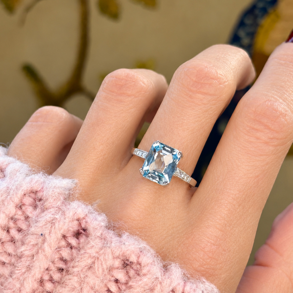 a model wearing a vintage style blue topaz and diamond ring in 9ct white gold